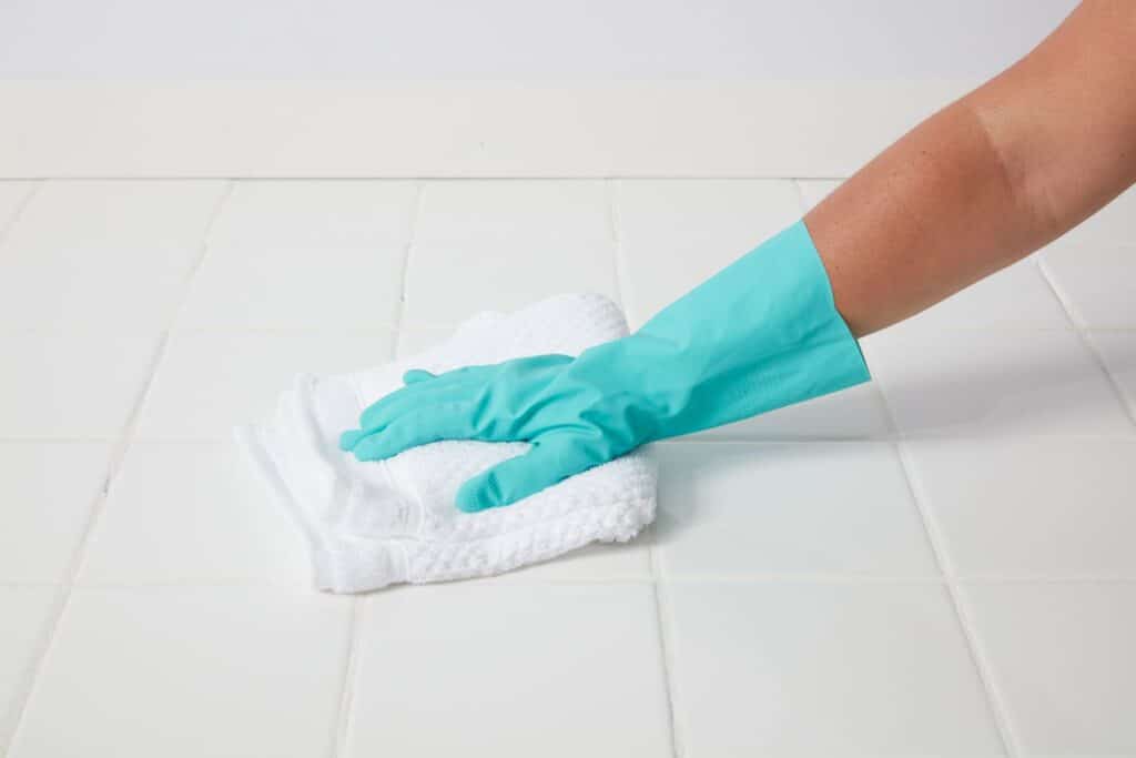 Gloved hand wiping clean white ceramic floor tile