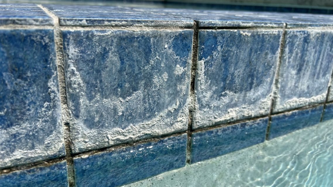 Close view of calcium scale bonded to blue pool waterline tile and grout before professional cleaning