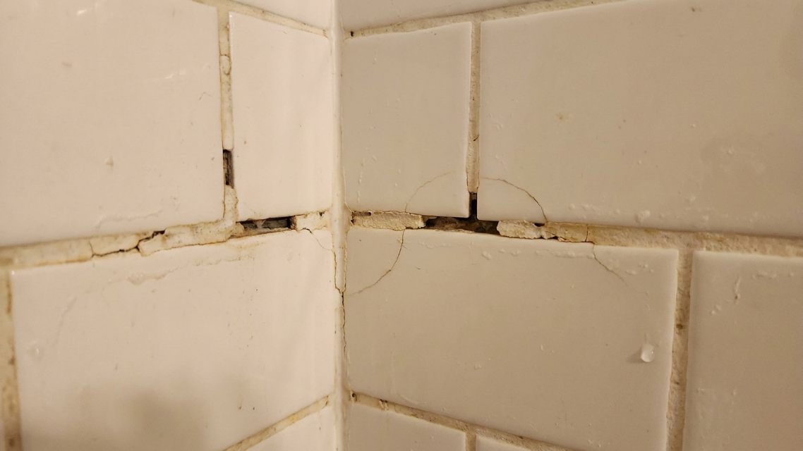 Close view of cracked and deteriorated grout in a shower corner before repair
